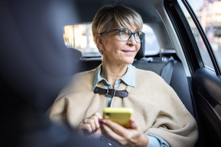 older woman in car looks out window smiling